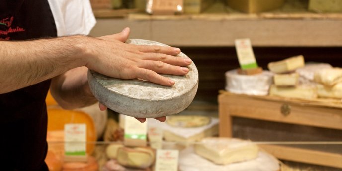 A cheese seller, or fromager, holds a roun of cheese in his hands while conducting cheese & Wine Tasting in a Paris Cheese Cellar