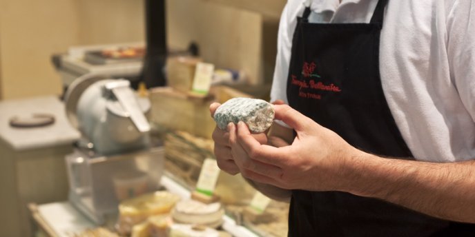 A cheese seller, or fromager, holds goat cheese in his hands while conducting cheese & Wine Tasting in a Paris Cheese Cellar