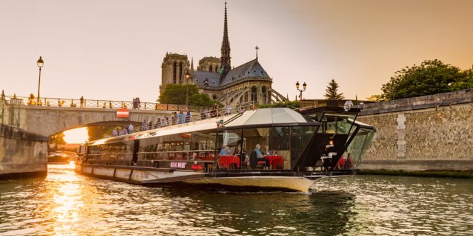 Bateau Mouche dinner cruise boat passing by Notre-Dame Cathedral on the Seine River in Paris at night