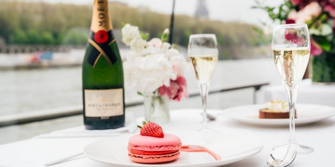 A close-up of macarons and champagne served n a Christmas lunch along the Seine River, with the Eiffel Tower visible in the background