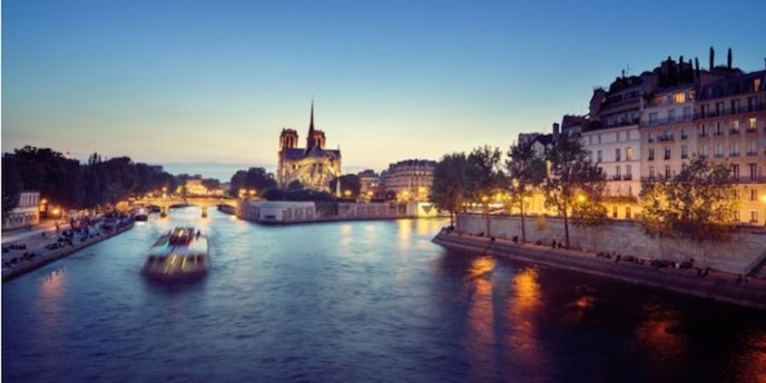 A river ruise boat at night with Notre Dame illuminated in the distance