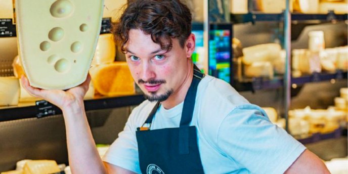 A cheesemonger in Paris holds a larged piece of cheese in th Marais in paris