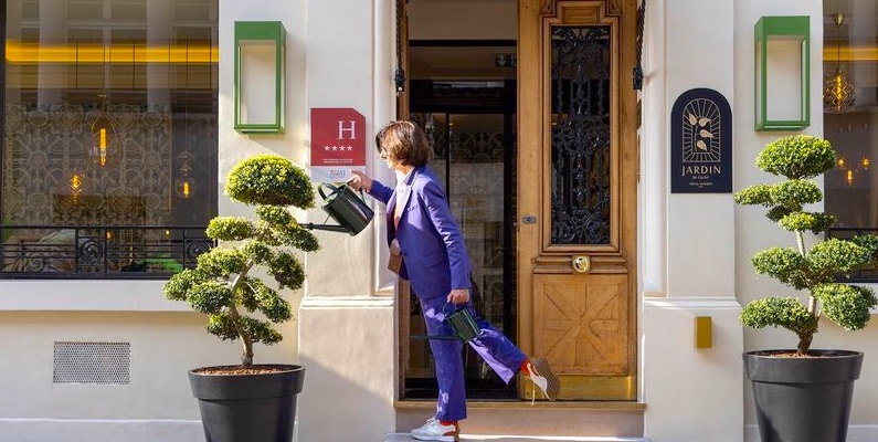 A soman waters plants in front of Hotel Jardin de Cluny