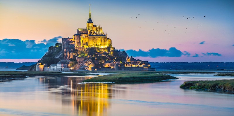 Mont Saint-Michel at night in a golden light, surrounded by water