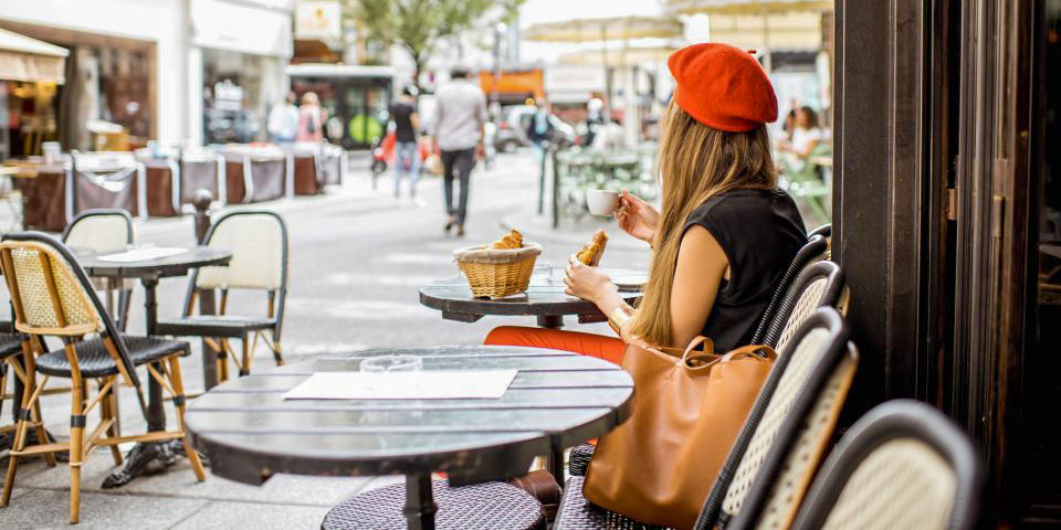 A woman in a red beret eats a croissant at a sidewalk table in Montmartre