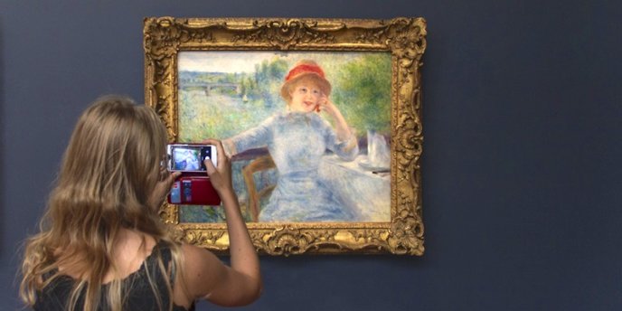 Young woman at Musee d'Orsay in Paris photographing a painting by Renoir