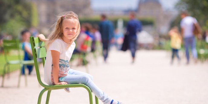 A yooung girl sits on a green chair in the Jardin de Luxembourg