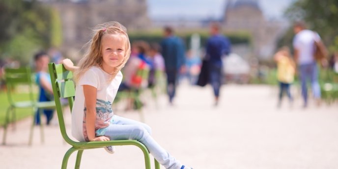 A young girl sitting on a chair in Tuileries in summer poses for the camera