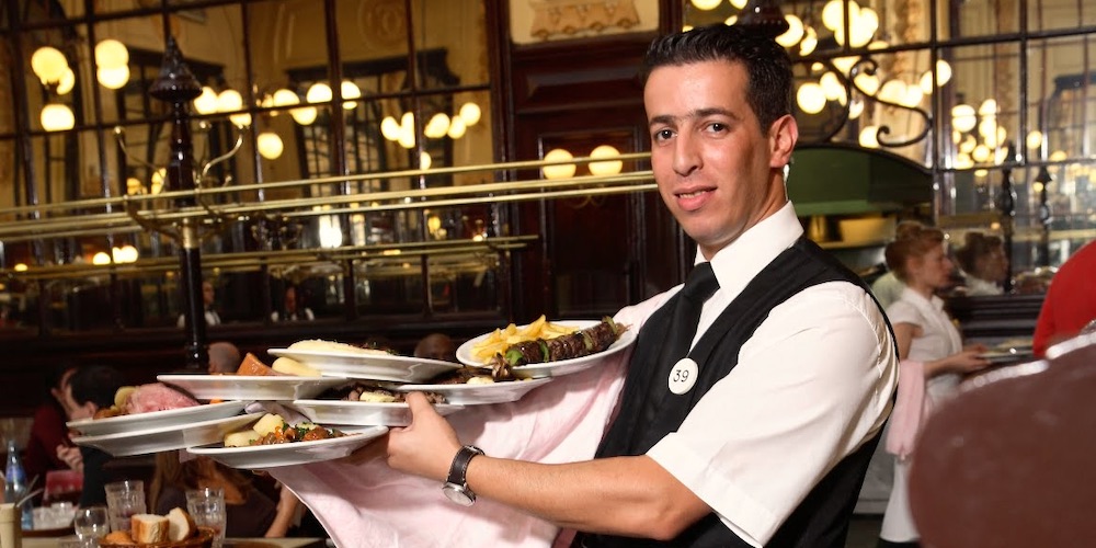 A server carries many plates to customers at Bouillon Chartier in Paris