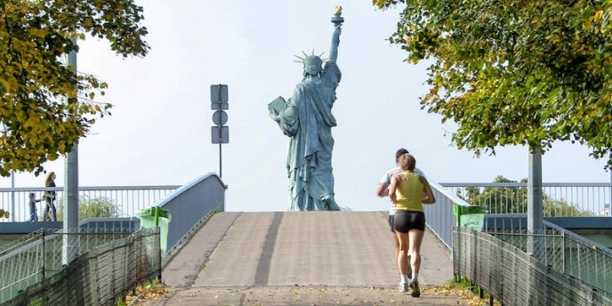 two runners approach the Statue of Liberty on Ile aux Cygnes on the river Seine in Paris