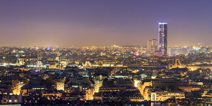 La Tour Montparnasse towers over Paris at night with the glowing lights of the city below