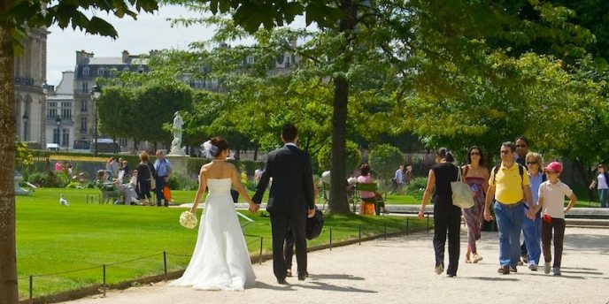 A bride in a long white wedding dress and a groom walking in the Tuileries in Paris