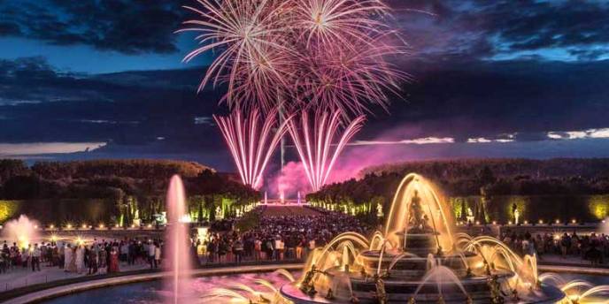 Nighttime view of the lighted fountains of Versailles with fireworks in the sky