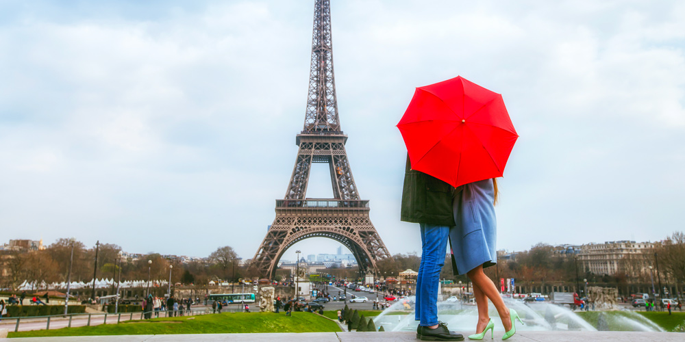 Under a red umbrella, a couple gazes at the Eiffel Tower on Valentines Day