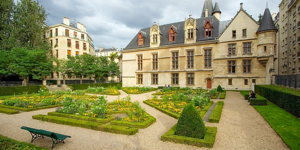 The garden of Hotel de Sens with paths, benvhes, and yellow flowersing plants