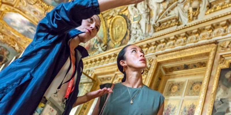 A tour guide explains the paintings at the Louvre on a guided tour