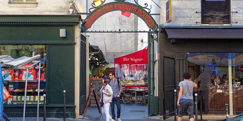 The arched entrance to Marché des Enfants Rouges with a red awning in the distance