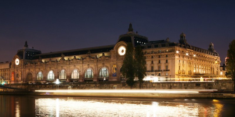 Musee d'Orsay exterior at night, lit up and reflected in the waters of the Seine