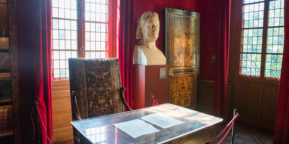 The study lined with red velvet walls and curtains, plus the writing desk