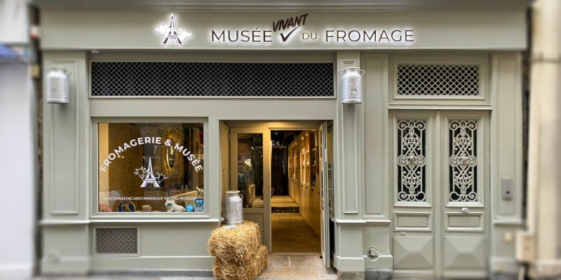 Musée du Fromage storefront using milk cans for lighting, with a hay bail by the door