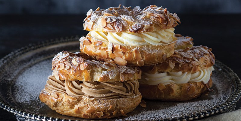 A stack of three pastries known as Paris Brest, wound like a bicyle wheel with sliced almonds on top and a creme filling