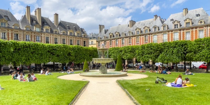 Place des Vosges on a sunny summer day, with people lounging on the grass and a fountain in the distance