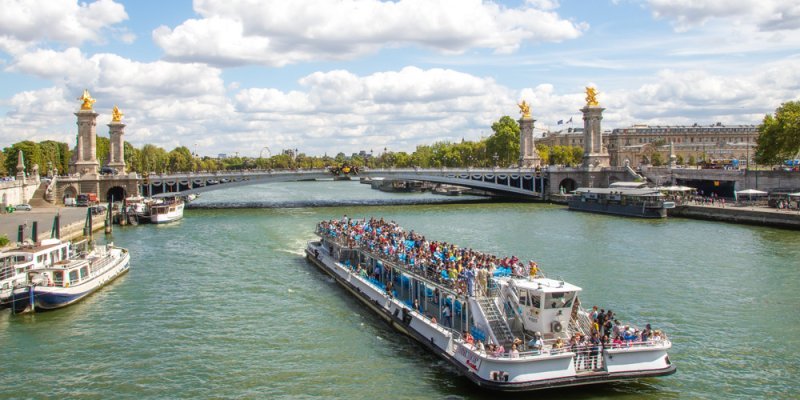 A river cruise boat approaches Pont Alexandre III Paris, seen with its four columns topped by golden statues