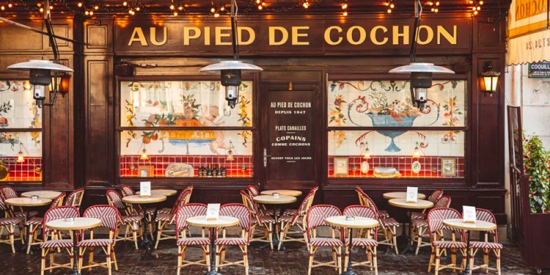 The exterior of Au Pied de Cochon with chairs and tables on the outdoor terrace